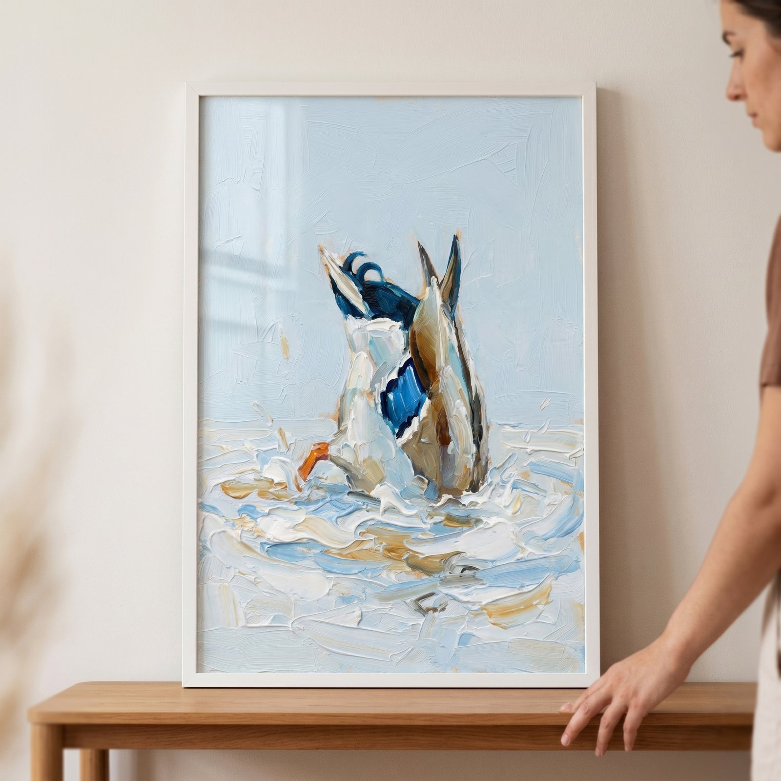 Whimsical bottoms up duck wall art in a white frame, showing a bird diving into textured blue and white water.