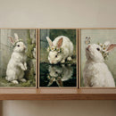 Whimsical daisy crown bunny wall art set of 3 on a shelf featuring white rabbits near moss, water, and a butterfly.
