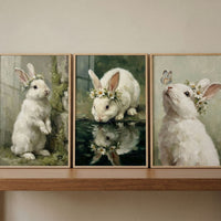 Whimsical daisy crown bunny wall art set of 3 on a shelf featuring white rabbits near moss, water, and a butterfly.