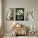 Whimsical daisy crown bunny wall art set of 3 above a dresser and bunny ear chair in a sage green nursery with a rug.