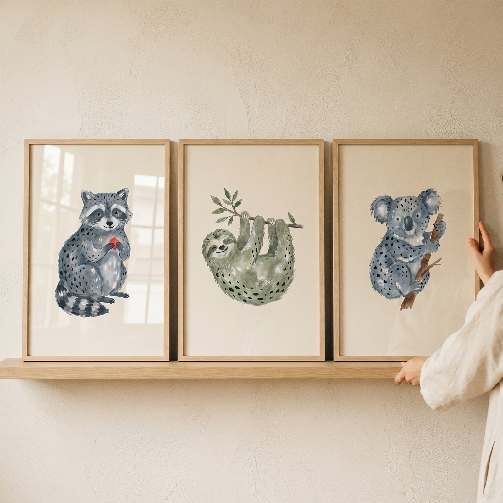 Whimsical earth tone animals wall art set of 3 featuring a raccoon, sloth, and koala framed on a wooden shelf.