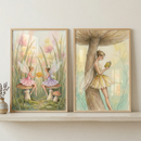 Two framed illustrations sit on a light wood shelf. The left artwork shows two small winged figures on mushrooms in a field of grass and flowers. One wears pink, the other purple, as they hold a golden object. The right piece depicts a winged figure in a yellow dress leaning against a large mushroom while reading a book. Both feature muted colors and delicate lines. The frames are light wood. To the left, a small vase holds dark sprigs.