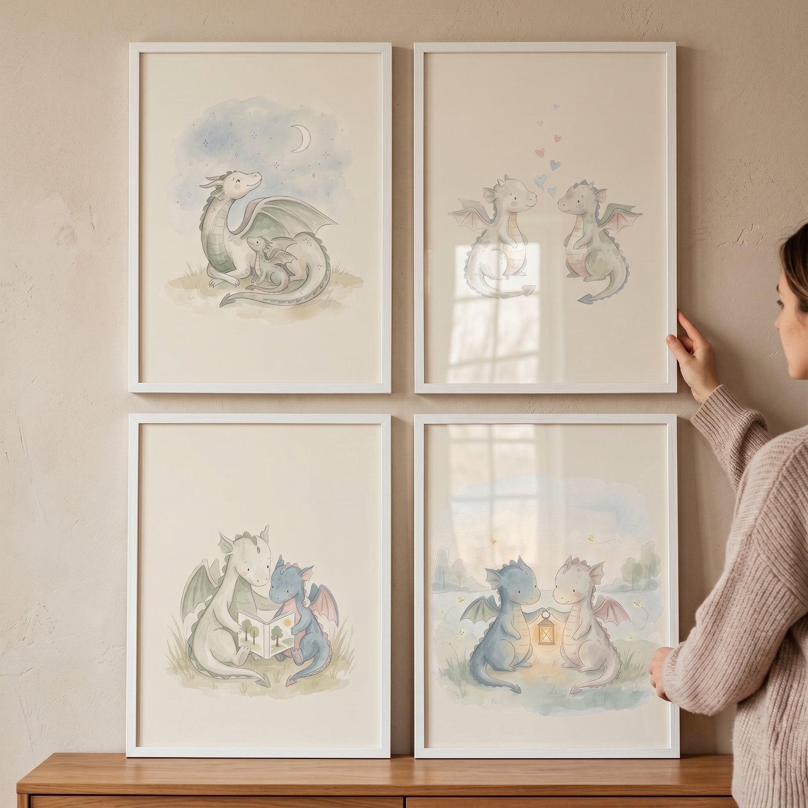Hands adjust a whimsical fairytale baby dragon wall art set of 4 framed watercolor illustrations on a neutral wall.