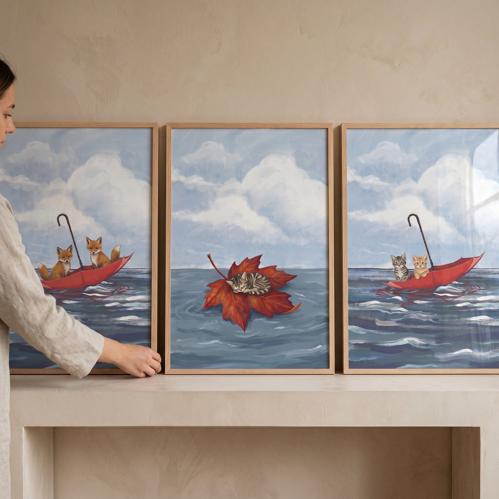 Whimsical floating baby animals wall art set of 3 shows foxes and kittens on a red umbrella and leaf being placed on a shelf.