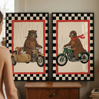 Two framed illustrations rest atop a wooden chest of drawers. Both artworks feature a black-and-white checkered outer border and a bold red inner frame. The left image depicts a brown bear wearing a leather pilot cap and goggles, operating a vintage motorcycle with a sidecar containing a map-reading squirrel. The right image shows a bear in similar attire with a long red scarf riding a green motorcycle. Thin vertical lines in the background suggest falling rain.