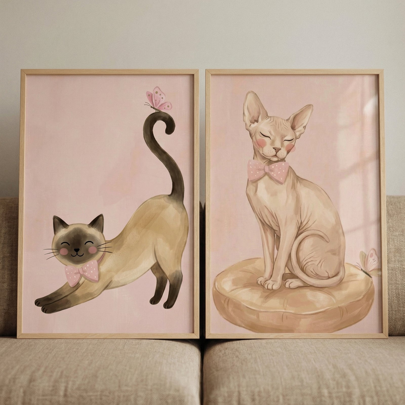 This pair of framed illustrations features whimsical, stylized cats in a soft, artistic style with light pink, textured backgrounds.

On the left, a cream-colored cat with dark brown ears, face, and paws is shown in a playful stretch. It has rosy pink cheeks and a gentle smile with its eyes closed. It wears a pink bow tie decorated with small white polka dots. A small pink butterfly is delicately perched on the tip of its long, curled dark tail.