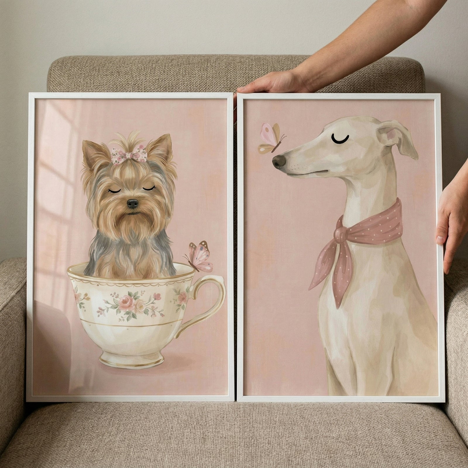 Two framed illustrations held by hands against a neutral backdrop. The left image features a small, fluffy dog with closed eyes and a pink bow, sitting inside a vintage-style floral teacup. A small pink butterfly rests on the rim. The right image shows a slender, light-colored dog with its eyes closed, wearing a pink polka-dot scarf tied around its neck. A butterfly hovers near its nose. 