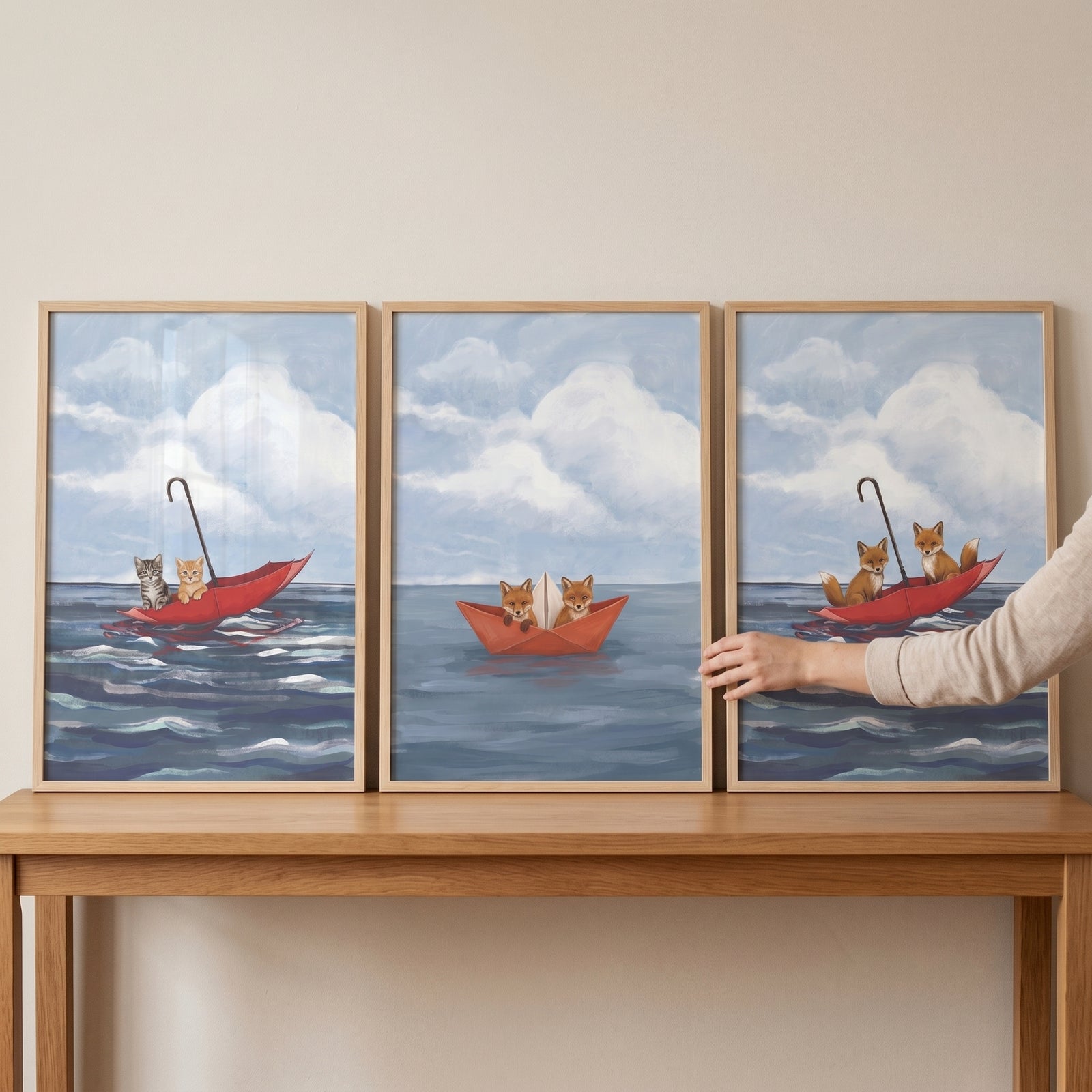 Hand touches a whimsical red boat animals wall art set of 3 featuring kittens and foxes in red boats on a blue sea.