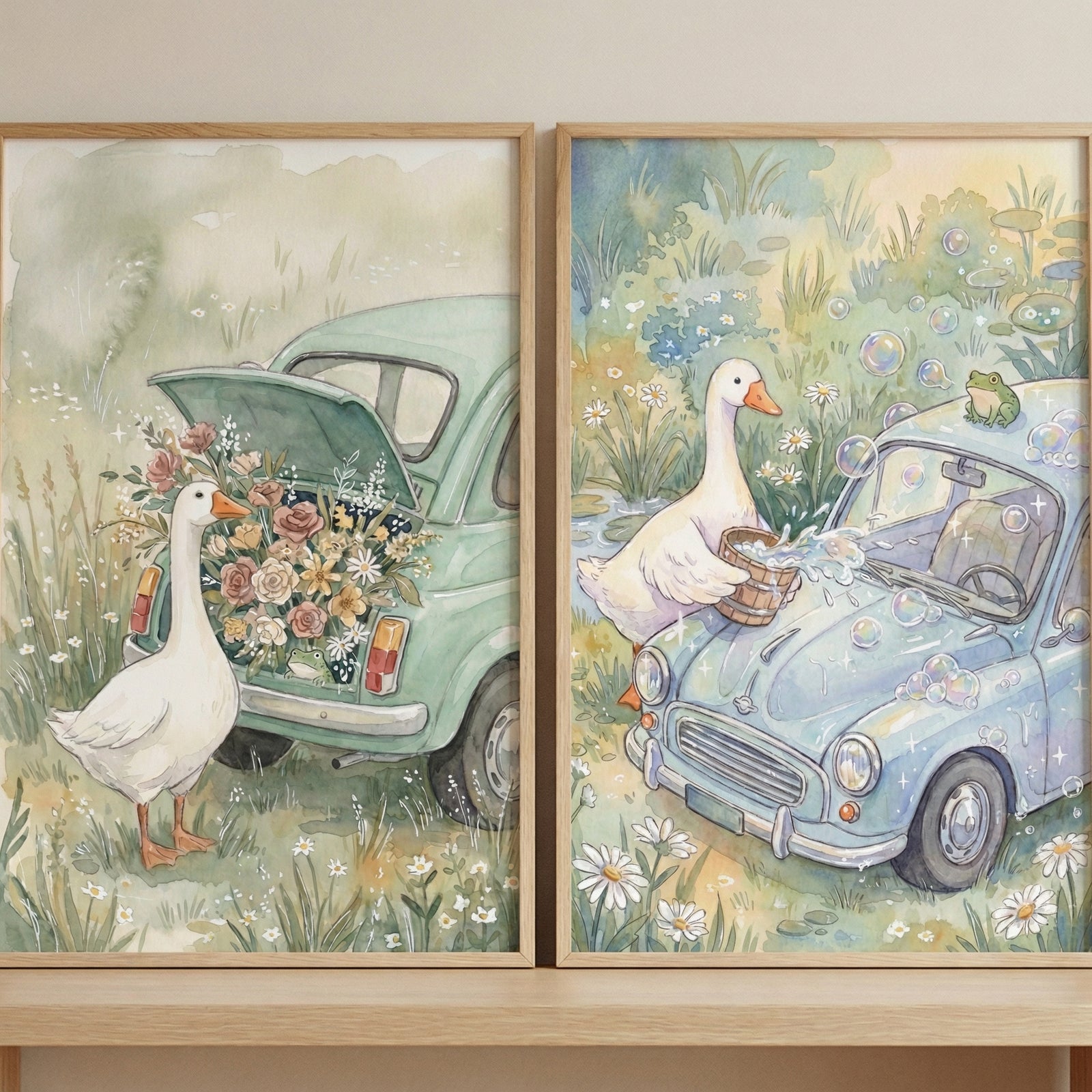 Two framed, whimsical watercolor-style illustrations are displayed side-by-side on a light-colored wooden shelf. Both pieces feature a soft, pastel color palette and a storybook-like charm. 
