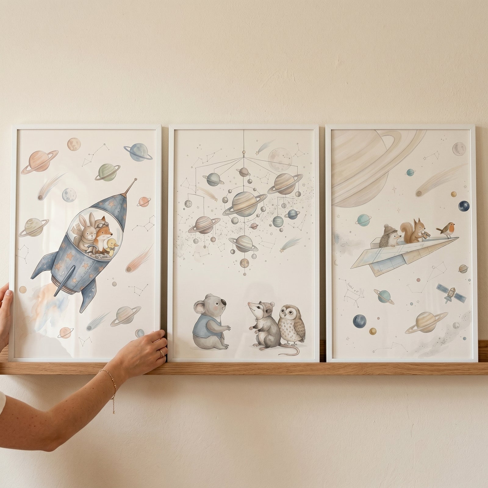 Whimsical watercolor cosmic animals wall art set of 3 on a wooden shelf being held by a hand.