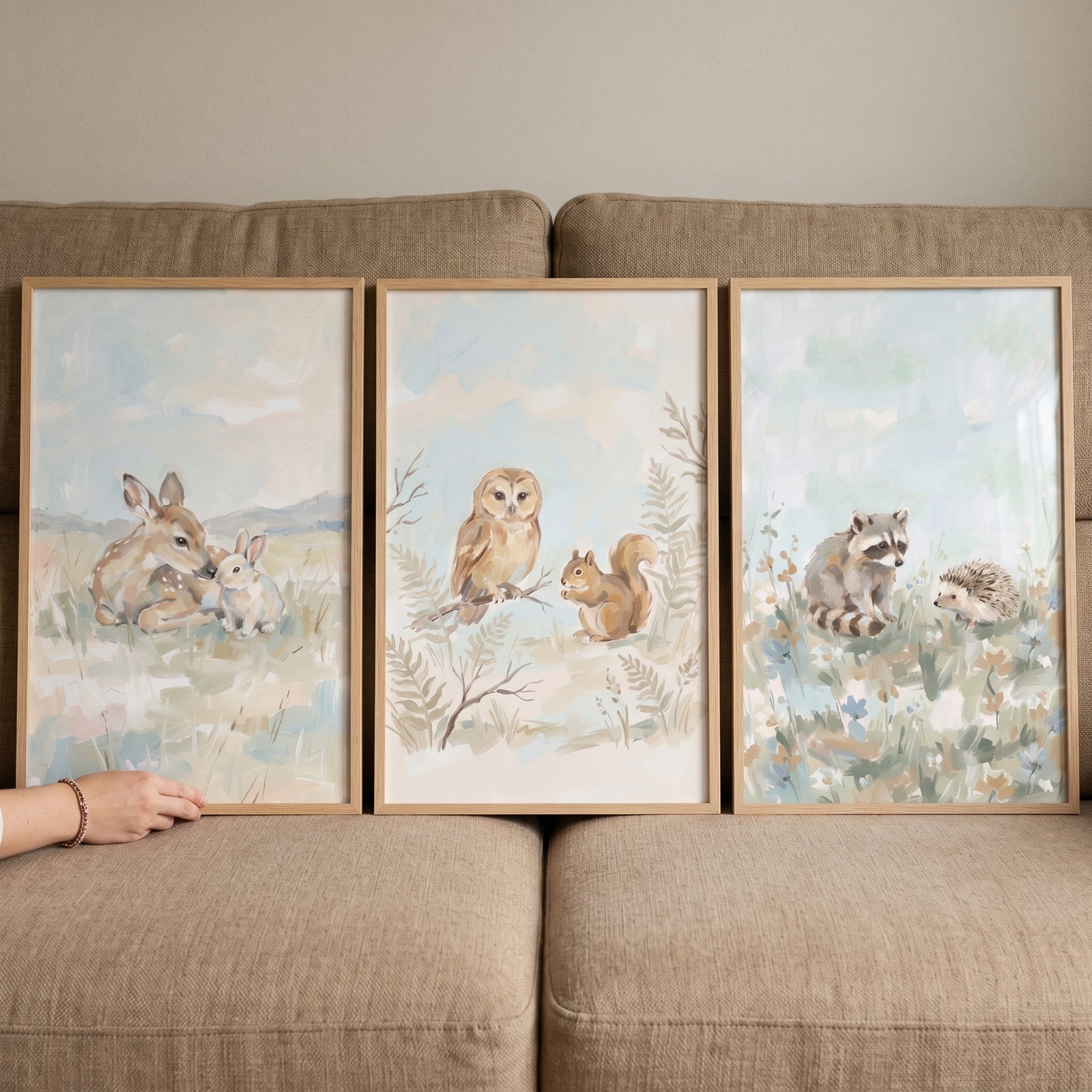 Whimsical watercolor woodland animals wall art set of 3 with a deer, bunny, owl, squirrel, raccoon, and hedgehog on a sofa.