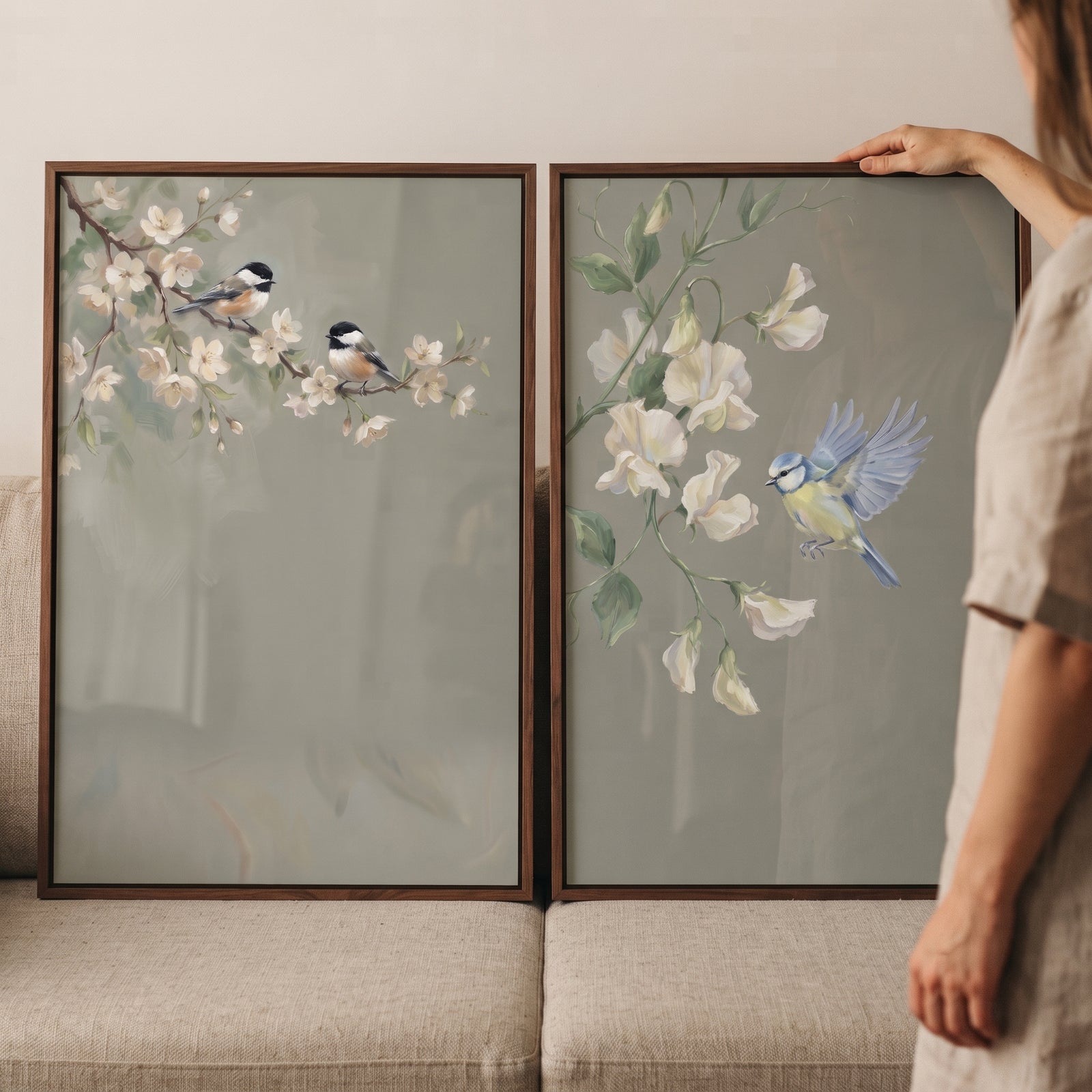White blossom garden bird wall art set of 2 showing birds on flowering branches in dark wood frames on a beige couch.