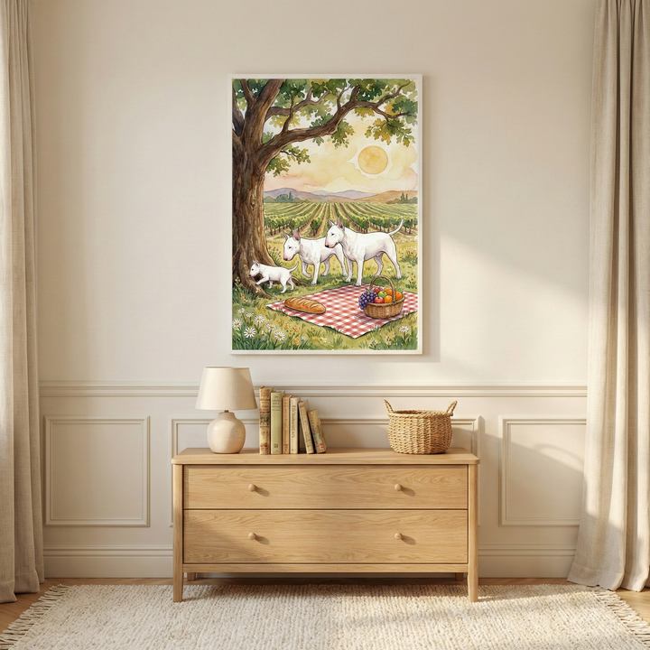 A cozy interior scene featuring a light-colored wooden dresser against a neutral wall with elegant paneling. Above the dresser hangs a large framed watercolor illustration of three white, egg-headed dogs on a picnic. The dogs are situated under a sprawling tree next to a red-and-white checkered blanket with a loaf of bread and a basket of fruit. The background shows a vast vineyard under a setting sun. 