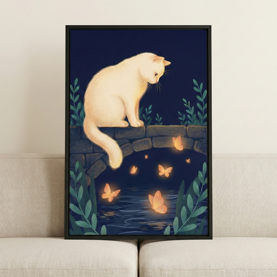 A framed illustration of a fluffy white cat sitting on a low stone bridge during the night. The cat is looking down at several glowing orange butterflies that are fluttering over the dark water visible beneath the bridge's arch. Stylized green plants grow on either side of the scene against a deep blue background. The framed artwork is propped up on a light-colored sofa against a neutral wall.