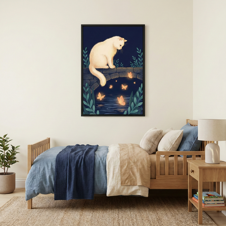 An interior view of a cozy bedroom featuring a wooden bed and a piece of wall art. A vertical rectangular framed artwork hangs on an off-white wall. It shows a soft, cream-colored cat perched on a dark stone bridge. Below the bridge, glowing orange butterflies flutter over dark blue water under a night sky. Stylized blue-green leafy branches frame the bottom corners of the illustration. The room includes a light-colored wooden bed, a nightstand with a lamp, and a potted plant.