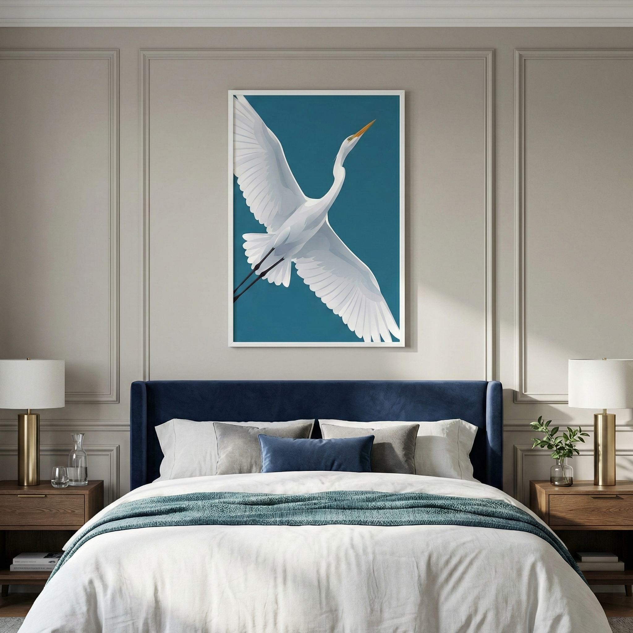A vertical framed artwork depicting a white egret in flight against a teal background is centered above a bed. The bed features a plush navy blue velvet headboard and is styled with white linens, a teal throw blanket, and a variety of pillows. The light taupe wall is decorated with classic panel molding. On each side of the bed, wooden nightstands hold gold-based lamps with white shades. The scene is elegant and calm, with soft natural light highlighting the coordinated decor.