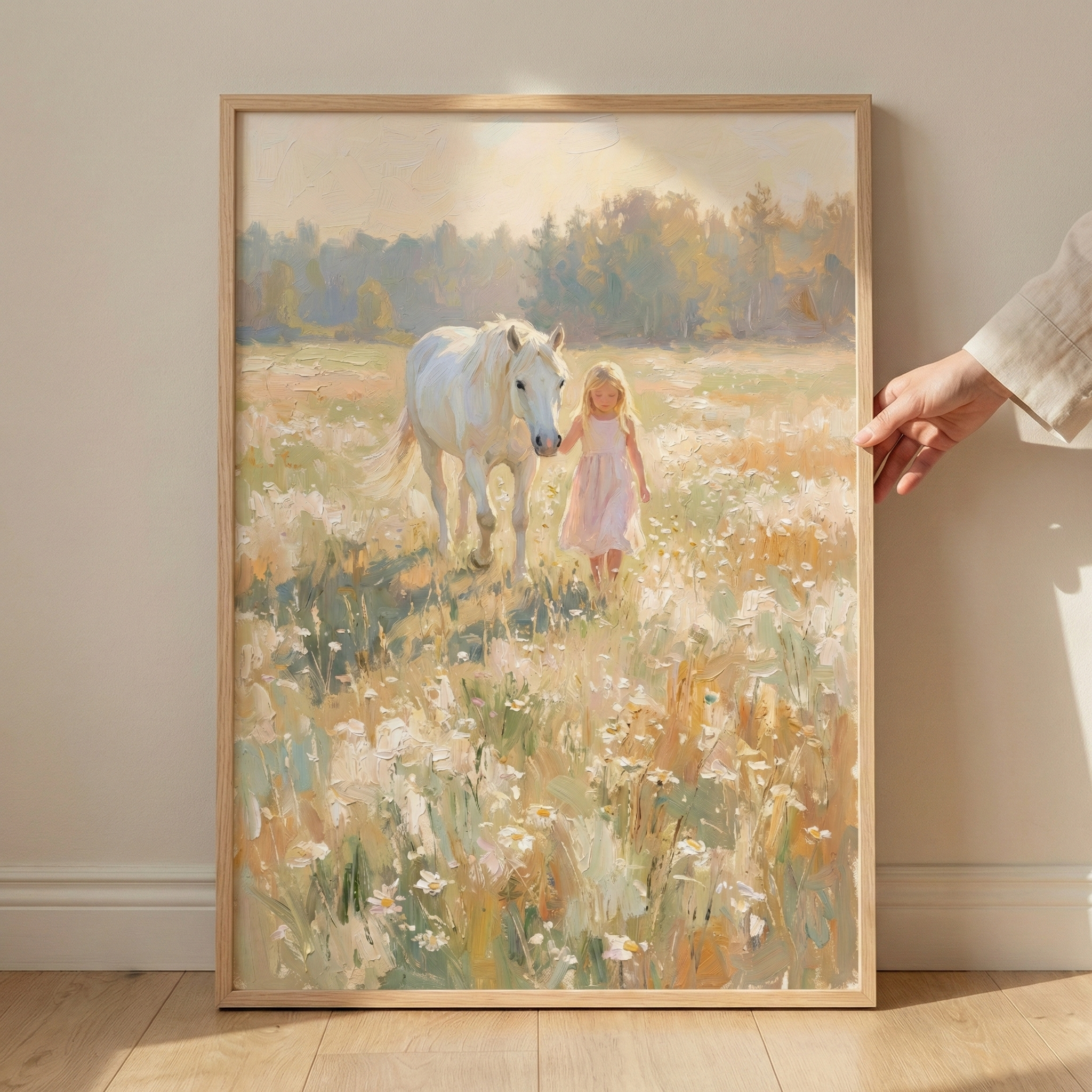 An impressionistic scene of a young girl with blonde hair in a soft pink dress walking beside a white horse. They are in a sunlit meadow filled with white wildflowers. The background shows a hazy forest under a bright sky. The artwork is in a light-wood frame, held by a person's hand against a neutral wall. The style features soft, textured brushstrokes and a serene, warm atmosphere with golden light. The entire composition has an ethereal, nostalgic quality.