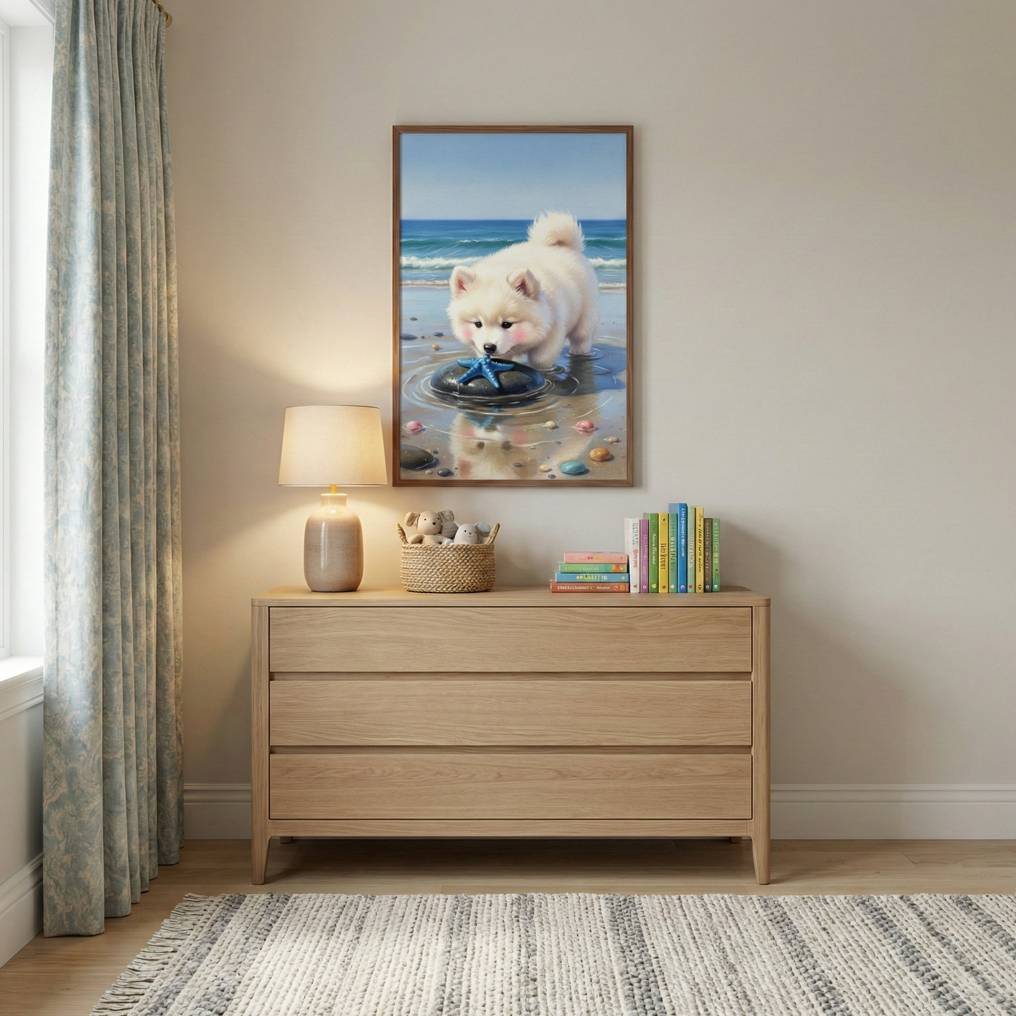 A bright, neutral-toned room features a light-colored wooden dresser set against a plain wall. On the dresser's surface is a small lamp with a neutral shade, a woven basket containing small plush toys, and several colorful books. Hanging above is a framed artwork of a small, fluffy white dog on a beach, looking at a blue starfish in a shallow pool. A window with patterned light blue curtains is on the left, and a striped, fringed rug lies on the floor in front of the dresser.