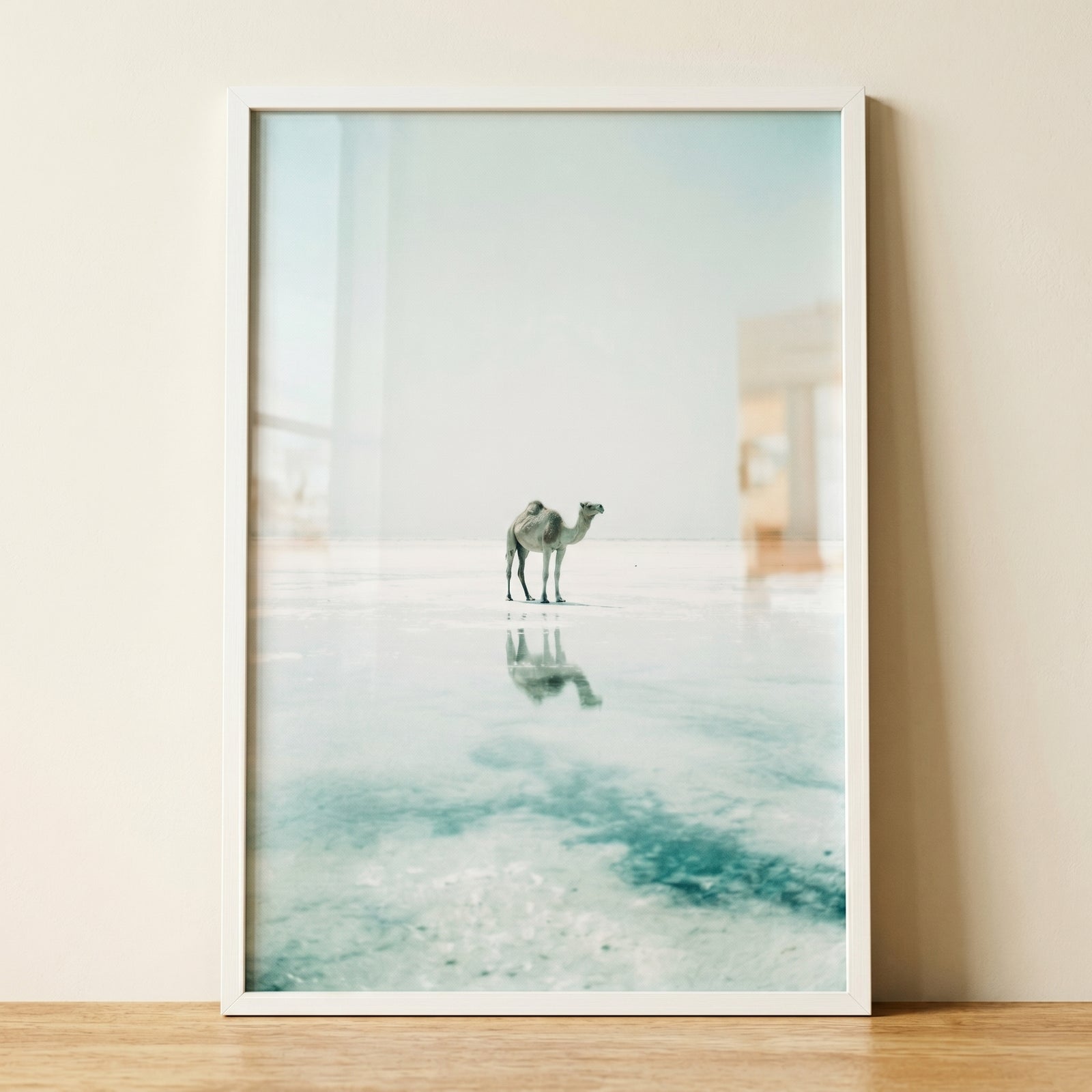 Framed white salt flat camel wall art depicts a lone camel and its reflection on a vast, pale expanse of water.