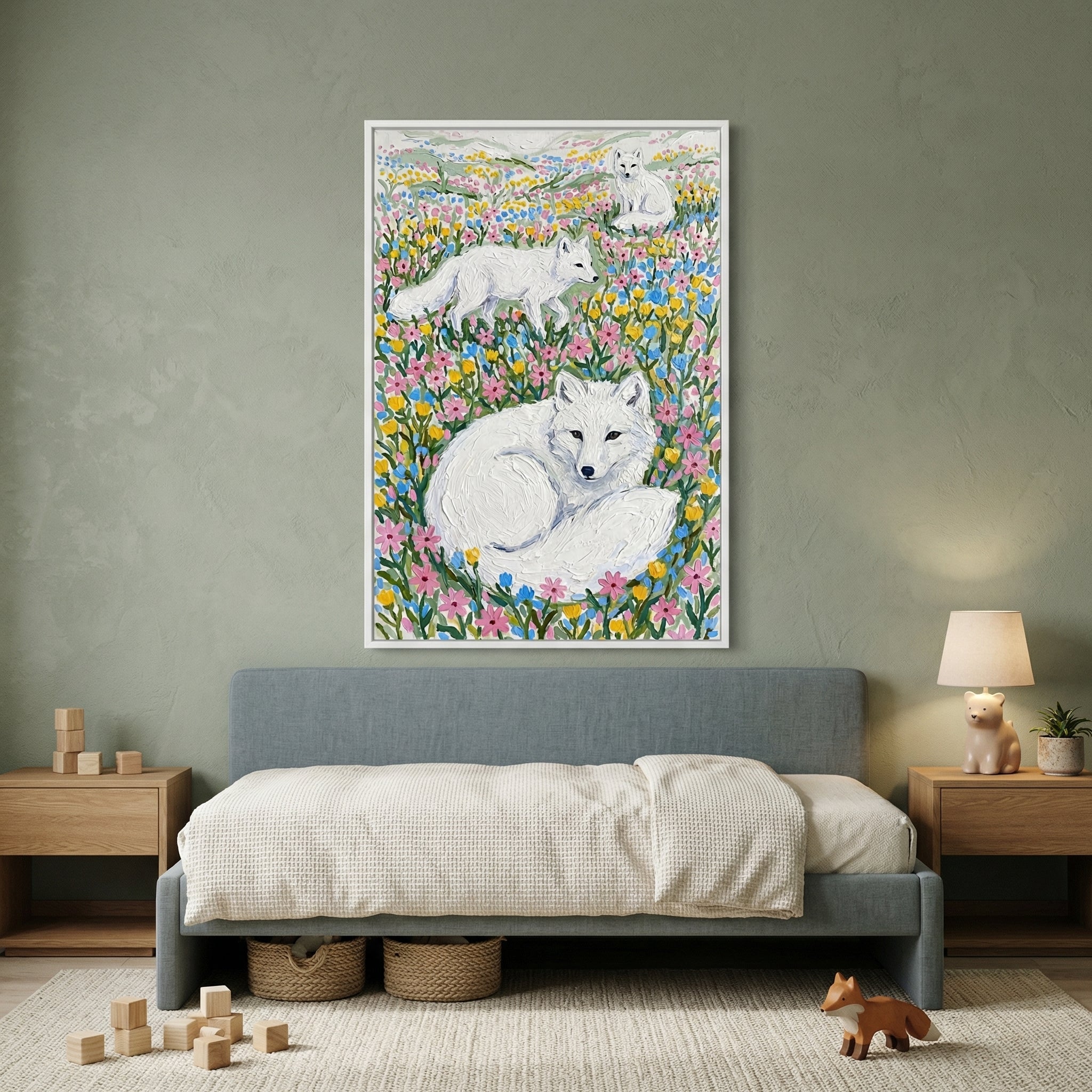 Framed painting of three white foxes resting and walking through a colorful field of pink yellow and blue wildflowers hangs above a low bed in a cozy child’s room. Soft textures wooden toys and warm lighting create a calm playful space that highlights the artwork.