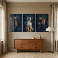 Three framed tiger prints hang above a wooden dresser in a styled living room. Each artwork shows a tiger in a different pose against a dark blue background with abstract topographic line patterns while a floor lamp, wooden toys, curtains, and a textured rug complete the warm interior setting.