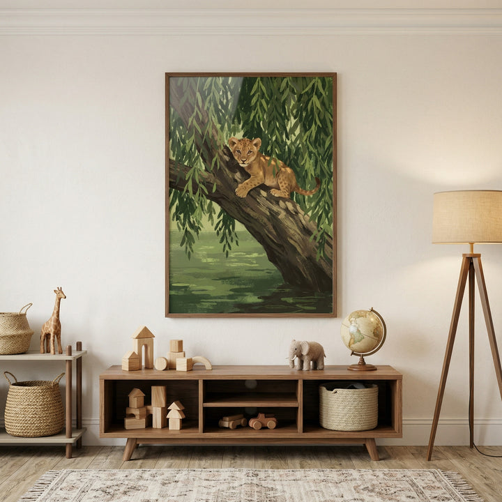 A large framed piece of artwork is the focal point on a plain white wall in a nursery or child's room. The illustration depicts a young lion cub perched on a large, textured tree branch that extends over a body of water. The background is filled with cascading green willow-like foliage, creating a lush, natural scene.
Beneath the artwork is a low, mid-century modern wooden console with open shelving. The shelves are neatly organized with various toys and decorative items: a collection of natural wood buil