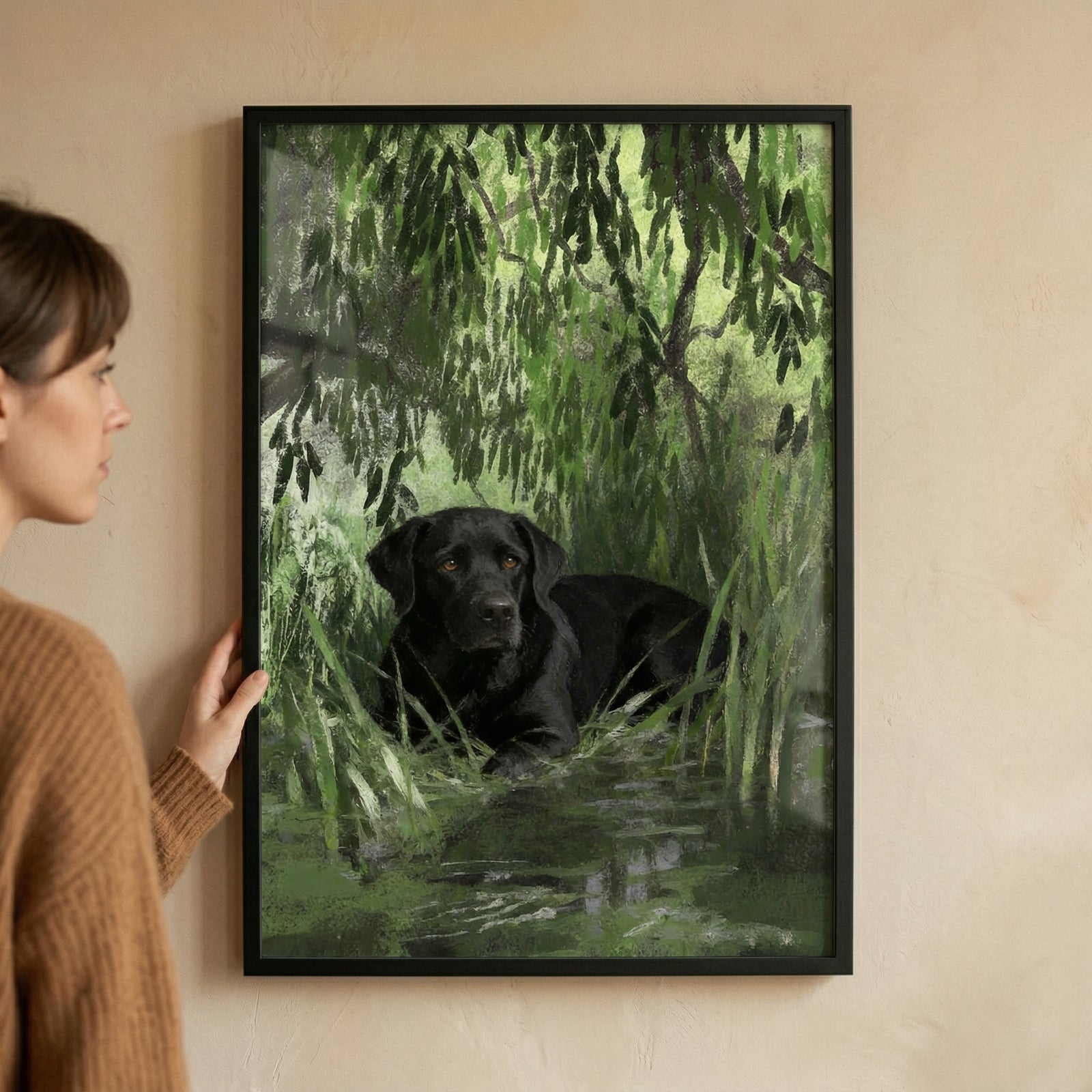Framed painting of a black labrador resting in shallow water surrounded by lush green foliage while a person holds the frame against a neutral wall. The rich greens and calm pose create a peaceful nature scene that adds depth and warmth to the space.