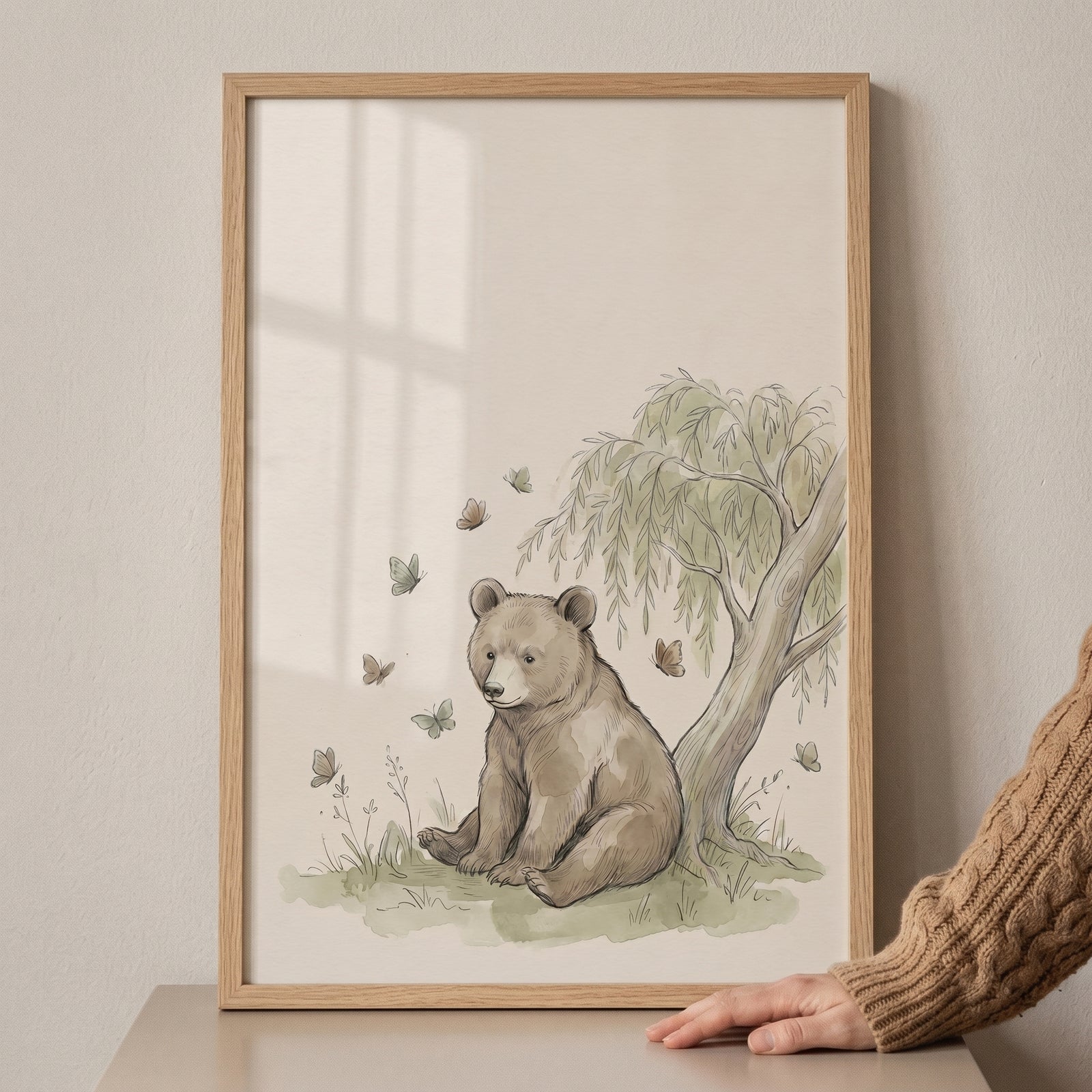 Willow tree sitting bear wall art in a light wood frame features a bear cub, butterflies, and soft green foliage.