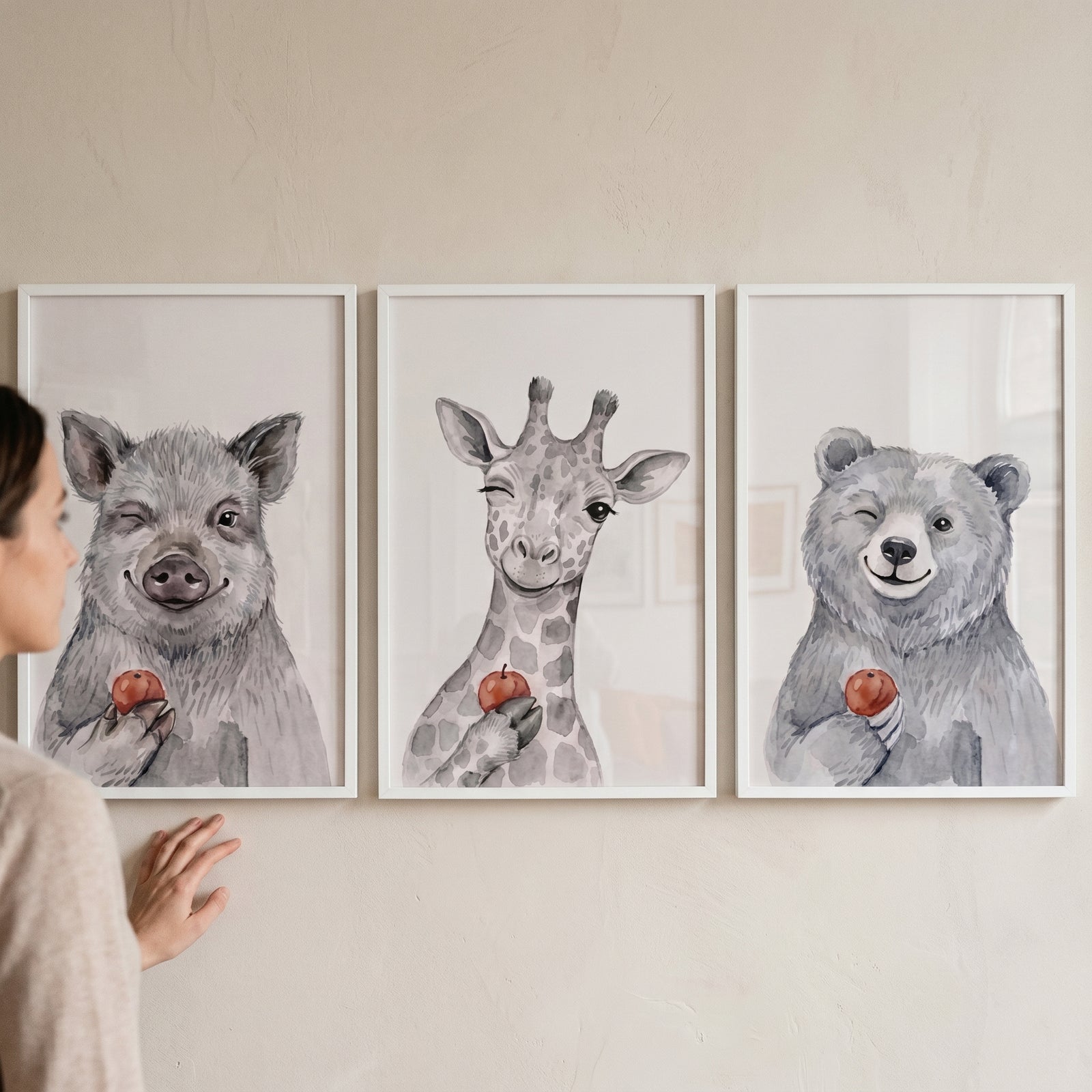 A person views a winking apple watercolor animals wall art set of 3 featuring a pig, giraffe, and bear.
