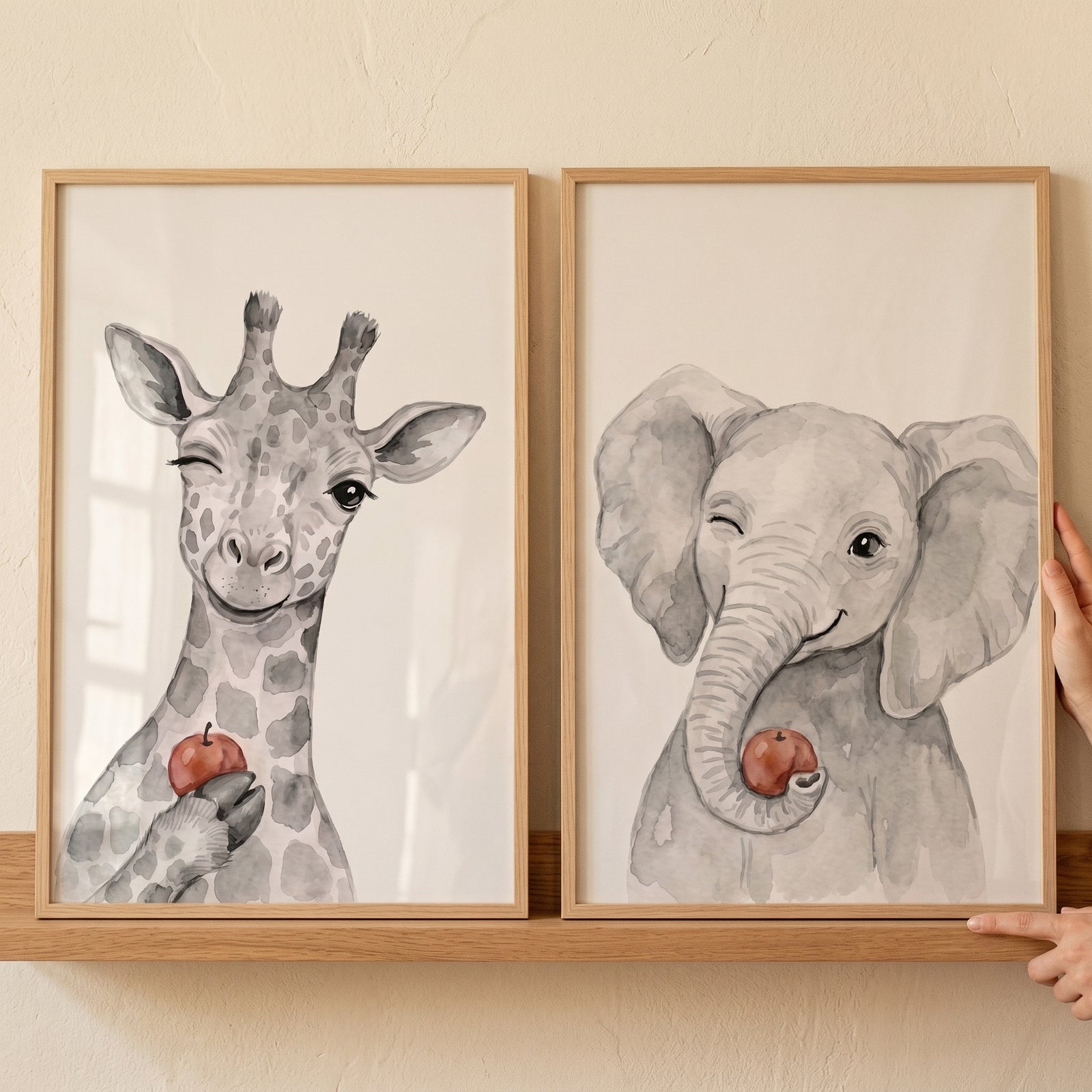 Framed giraffe and elephant illustrations in a winking red apple animals wall art set of 2 on a wooden shelf.