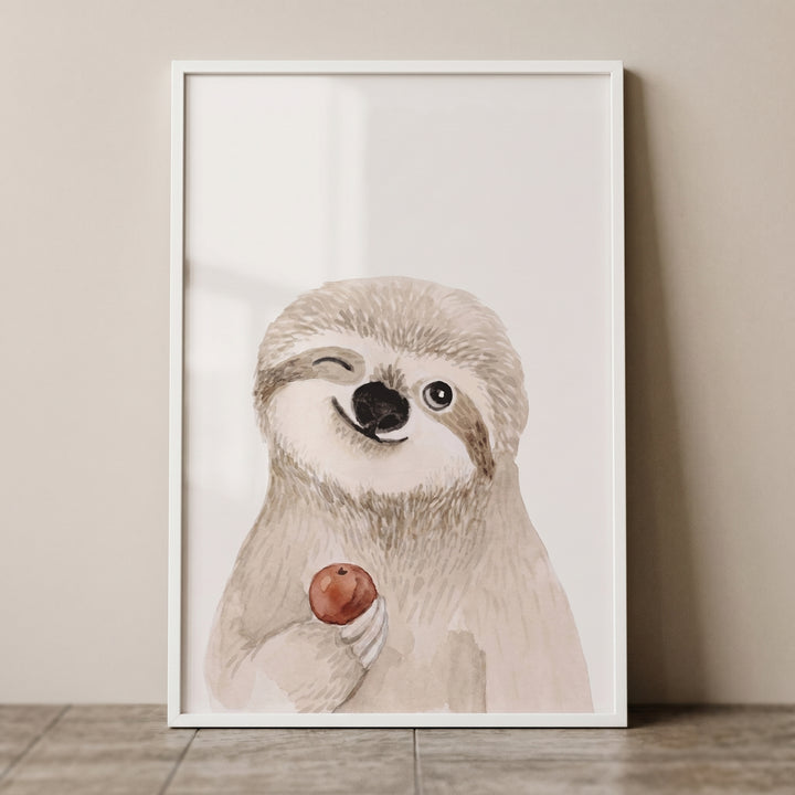 Watercolor winking red apple sloth wall art in a white frame leaning against a neutral wall.