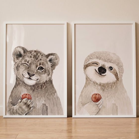 Two framed illustrations of a leopard and a sloth in this winking red fruit animals wall art set of 2.