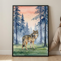 A vertical framed watercolor illustration featuring a solitary wolf standing in a misty forest. The wolf has detailed fur in shades of brown, tan, and gray, looking back over its shoulder. Behind the animal, tall blue-toned pine trees rise into a soft pink and orange gradient sky. Small silhouettes of birds fly in the distant sky. The foreground shows green grass with delicate brushstrokes. The artwork is set in a thin black frame, leaning against a white wall on a light wood floor.