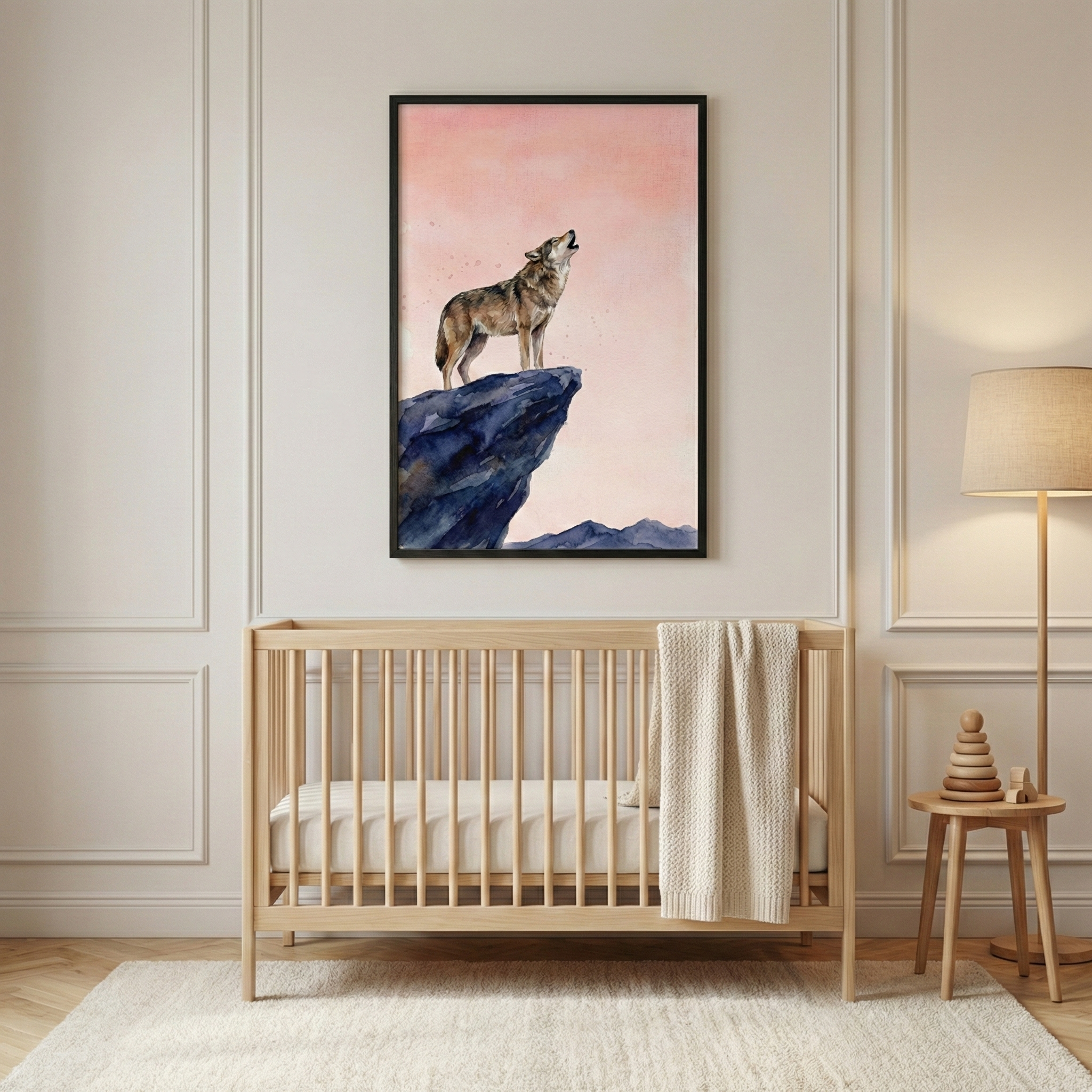 A portrait-oriented framed artwork hangs on a light beige wall featuring decorative panel molding. The art illustrates a brown and grey wolf howling from the edge of a jagged blue cliff under a soft pink sky. Below the art sits a light-toned wooden crib with vertical slats, holding a neutral-colored mattress and a cream knitted blanket draped over the railing. To the right, a simple floor lamp with a neutral shade stands next to a small wooden side table holding a stacked wooden toy.