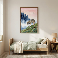A vertical watercolor artwork is framed and hung on a minimalist bedroom wall. The art features a wolf walking down a green and brown grassy slope. In the background, dark blue coniferous trees are partially hidden by a thick white fog under a soft, peachy sky with several small birds flying in the distance. The piece is in a simple wood frame above a light-colored wooden bed with sage green and cream bedding. A small wooden nightstand with a lamp and books sits nearby on a woven rug.