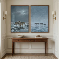 Wooden console table with a bowl and stacked books beneath two framed winter wolf paintings. One painting shows two adult wolves and a pup walking through icy water under a cloudy moonlit sky while the other shows two adult wolves and a pup crossing a frozen lake in pale blue fog.