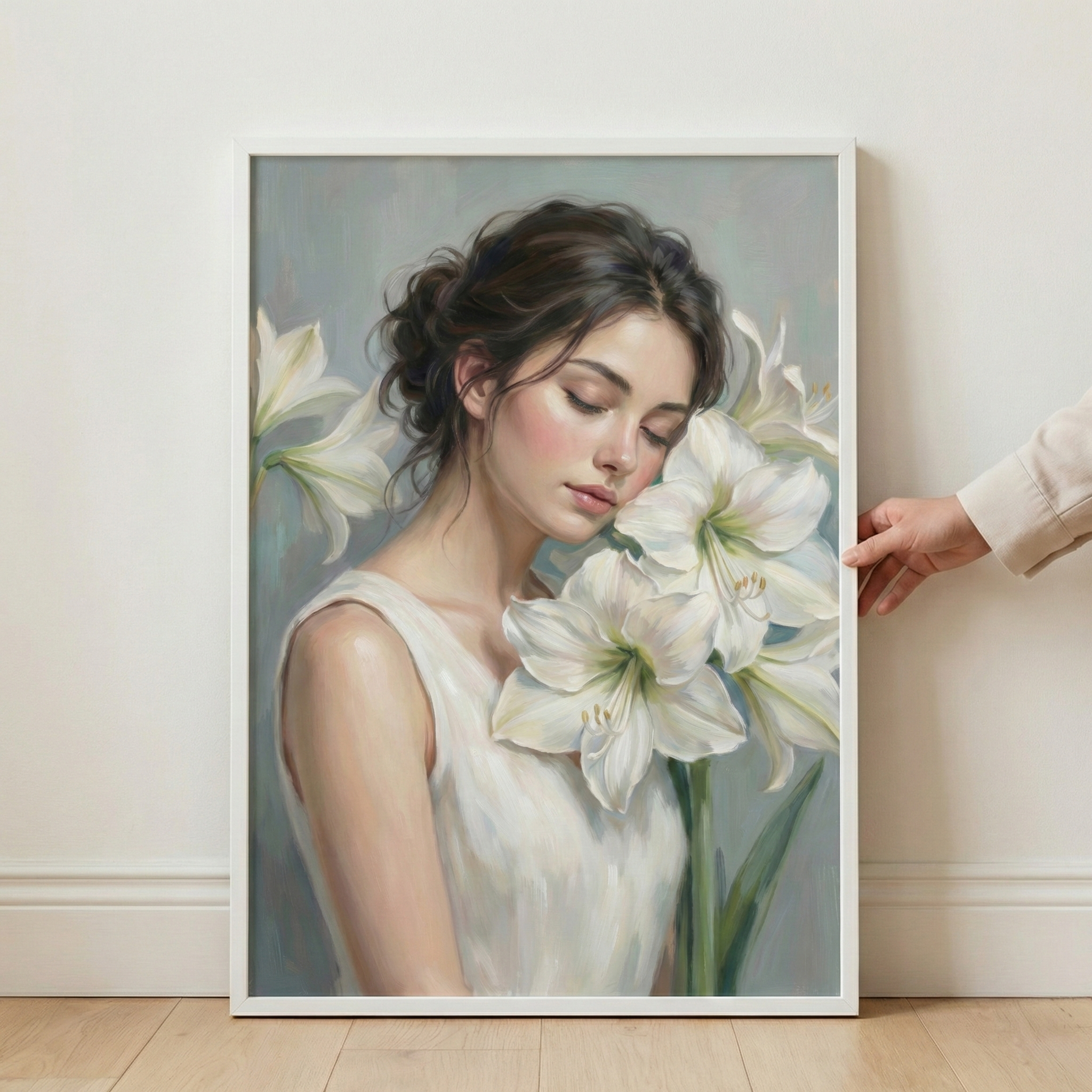A framed artwork displays a serene portrait of a young woman with dark hair in a loose bun and a peaceful expression, her eyes gently closed. She is surrounded by several large, blooming white flowers with delicate petals and long green stems. She wears a simple, light-colored sleeveless garment. The piece features a soft, expressive brush-stroke style. The white rectangular frame is shown leaning against a white wall on a wooden floor, with a hand visible on the right side.