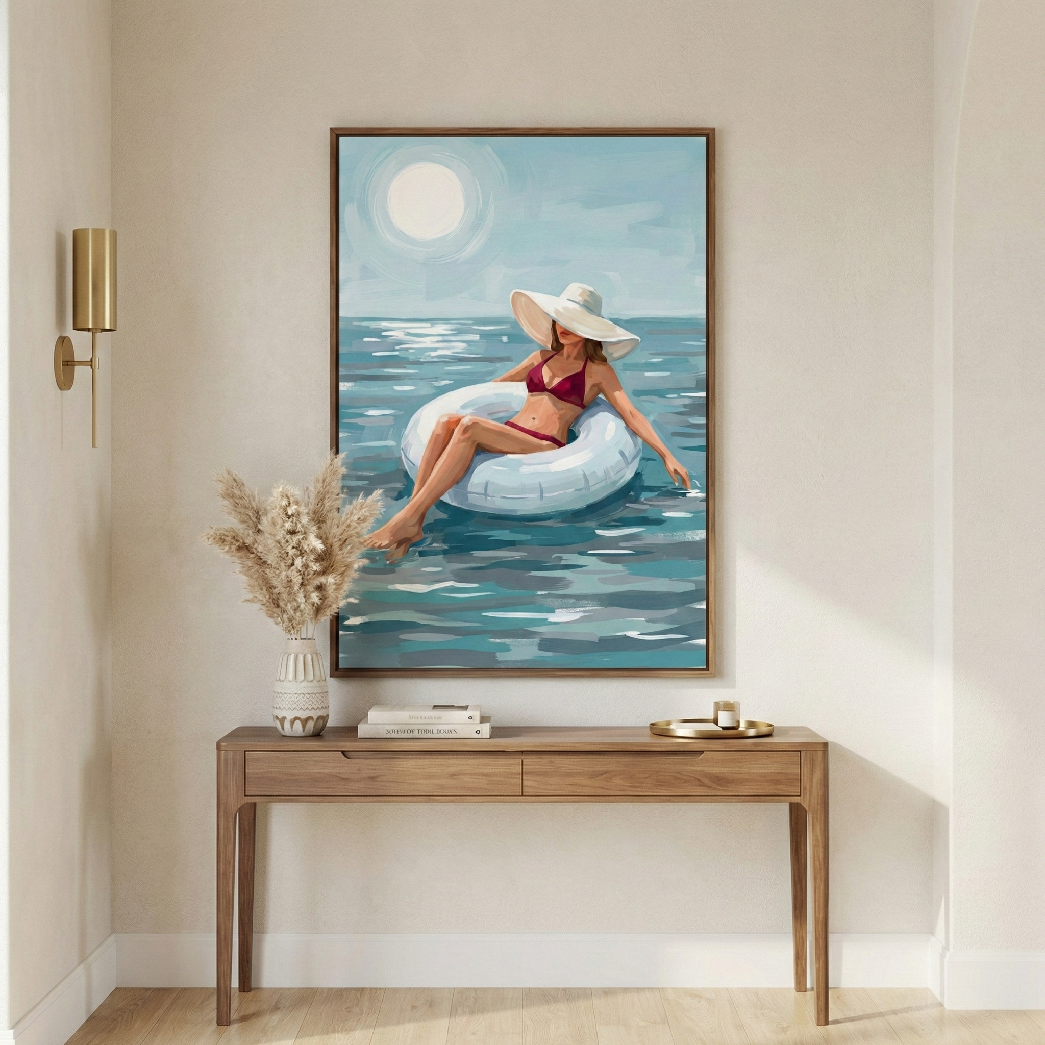 This image features a rectangular framed piece of art hanging on a neutral-colored wall above a wooden console table. The artwork depicts a woman wearing a red bikini and a large white sun hat, lounging in a white inflatable inner tube on a body of water with shades of blue and green. A large, pale sun shines in the light blue sky above the scene. The style of the artwork is characterized by prominent, visible brushstrokes that create a sense of texture and light. 
