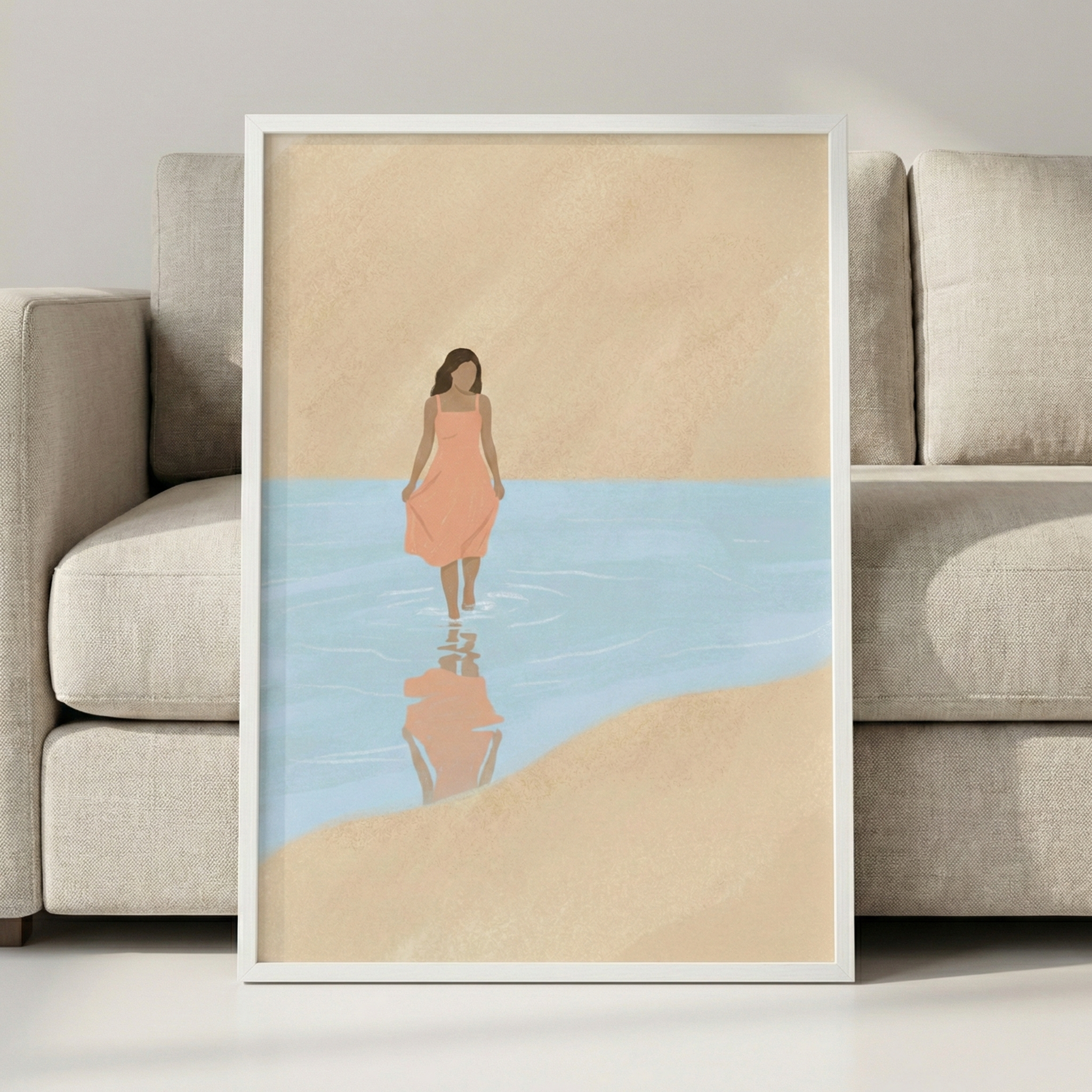 A minimalist digital illustration shows a woman with long brown hair, wearing a peach-colored midi dress, walking through shallow, light blue water. Her reflection is visible on the surface of the water below her. The setting is a simple beach landscape with warm, tan-colored sand in the foreground and background. The figure is depicted in a faceless, modern style with soft, clean lines. This piece is presented in a white frame, leaning against a textured, light-colored sofa in a bright room.