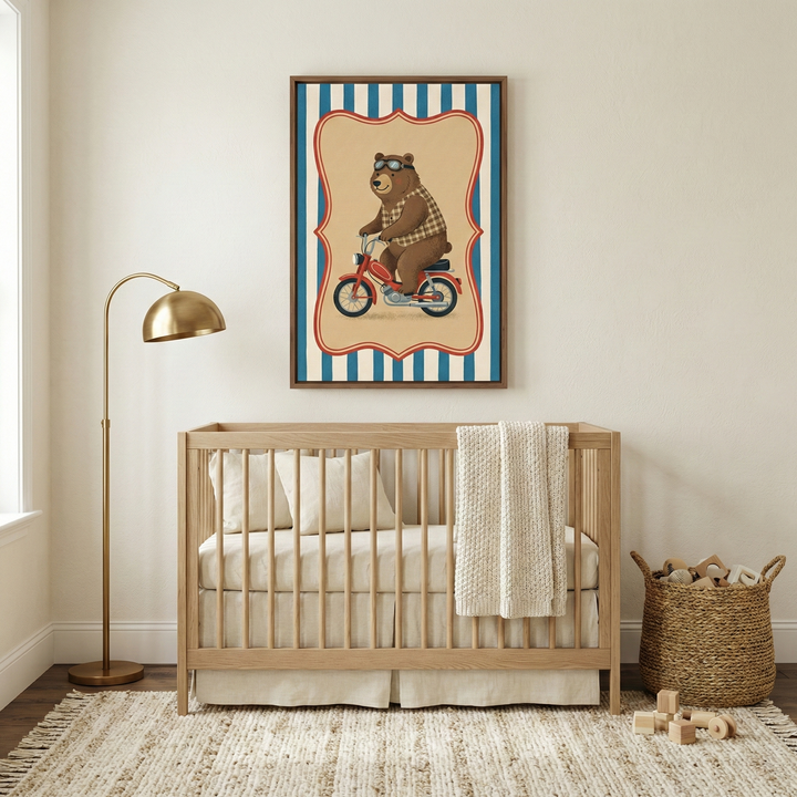 A cozy, neutral-toned nursery features a light wood spindle crib against a cream wall. Centered above the crib is a framed illustration of a brown bear in goggles and a checkered vest riding a red motorcycle, set within a red-bordered frame on a blue and white striped background. A gold arc floor lamp stands to the left, and a woven basket filled with wooden toys sits on the right. A textured, fringed rug lies on the dark wood floor with several wooden blocks nearby.