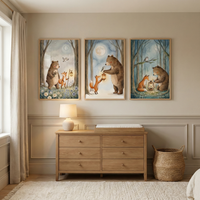 Neutral nursery room with three framed watercolor woodland prints hanging above a light wood dresser. The artwork features a bear and fox holding glowing lanterns in a moonlit forest, styled in soft blue and earthy tones that complement the beige walls, woven basket, table lamp, and cozy textured rug.