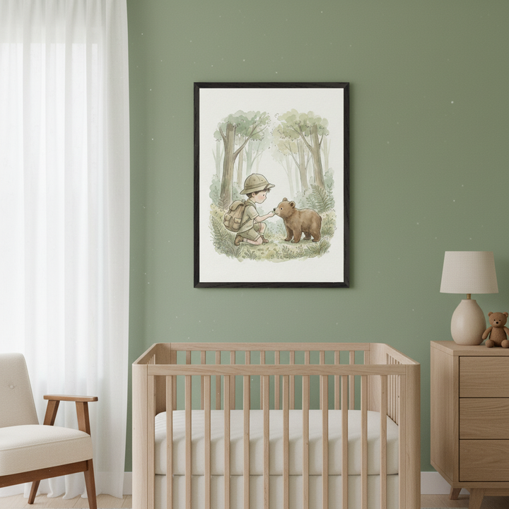 Modern nursery with a light wood crib and dresser against a sage green wall. A framed watercolor illustration of a boy and a bear cub in a forest hangs above the crib.