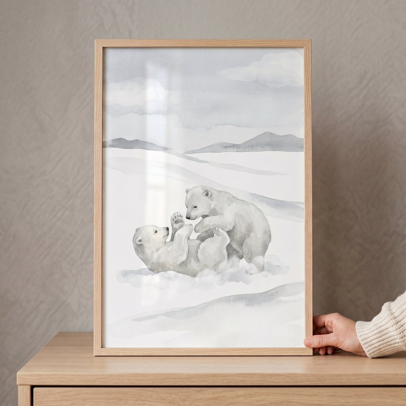 Wrestling snowy polar bear wall art featuring two bear cubs playing, framed on a wooden dresser and held by a hand.