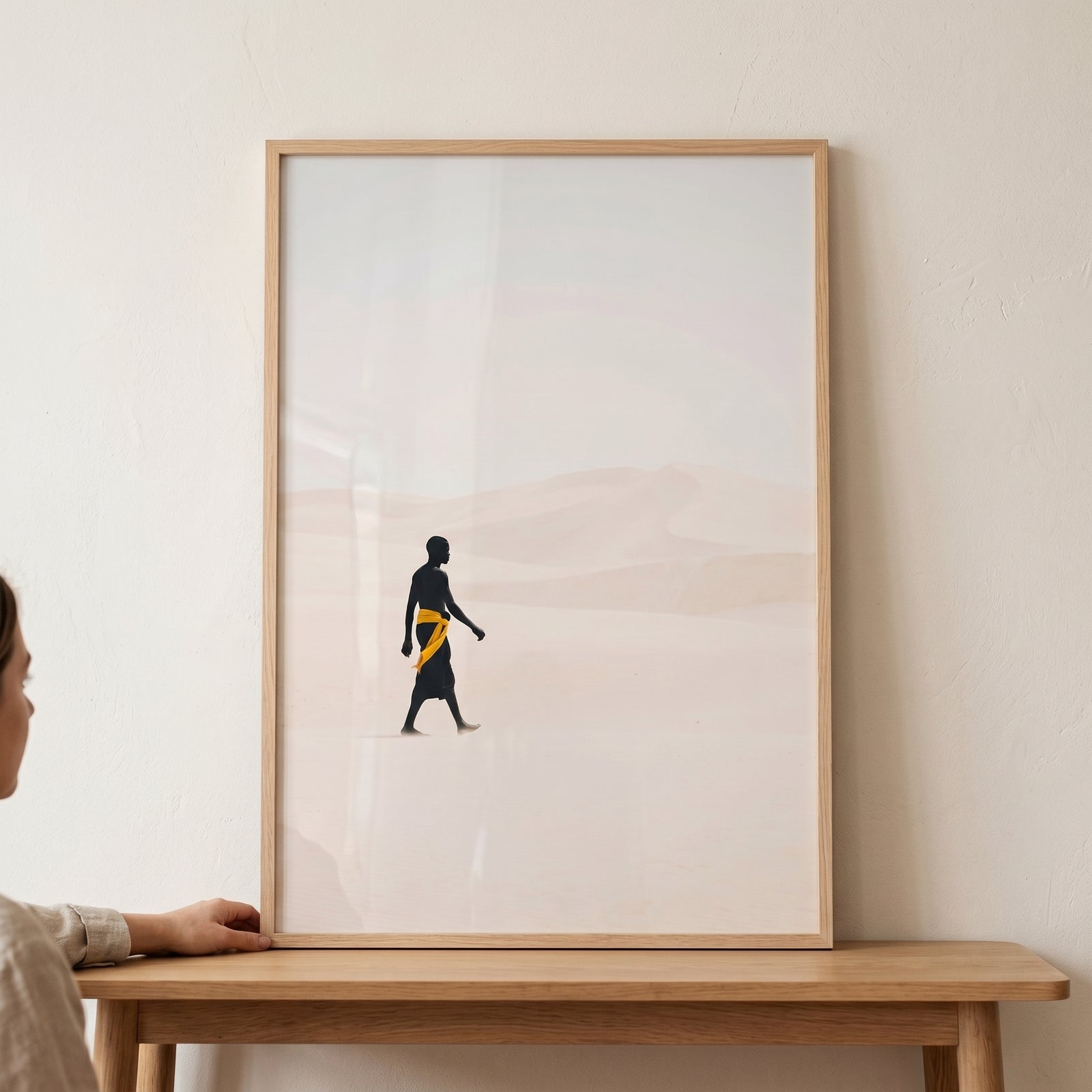 Yellow sash walking man wall art shows a silhouette traversing a minimalist desert landscape with soft beige dunes.