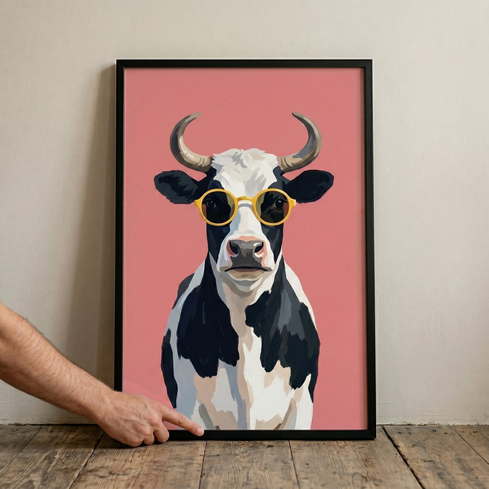 Yellow sunglasses funky cow wall art of a black and white cow on a pink background, held in a black frame.