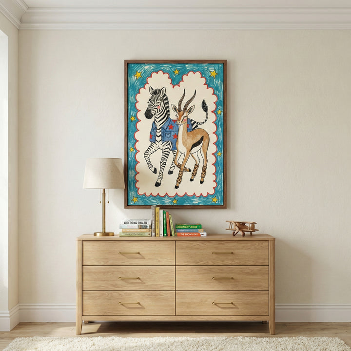 Framed artwork of a zebra and antelope in quirky outfits displayed above a wooden dresser in a cozy, neutral-toned room with children's books and a toy airplane on top.